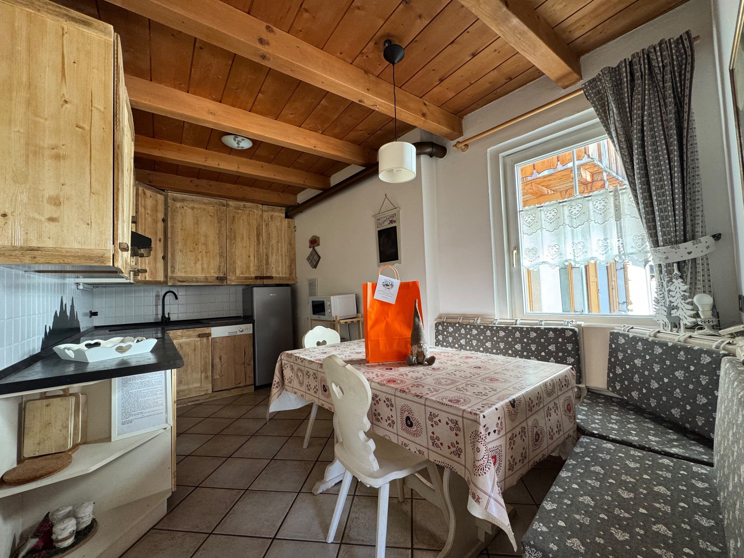 Zona pranzo della cucina con panca angolare e finestra con tende