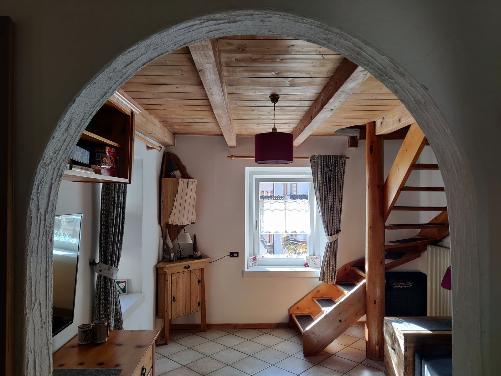 Soggiorno visto attraverso l’arco, con scala in legno e finestra sul paese